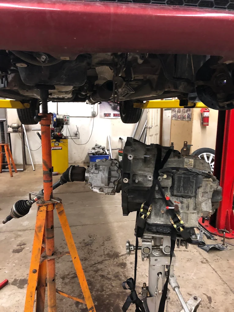 Driveshaft and gearbox lowered on a jack beneath a vehicle during suspension and drivetrain work